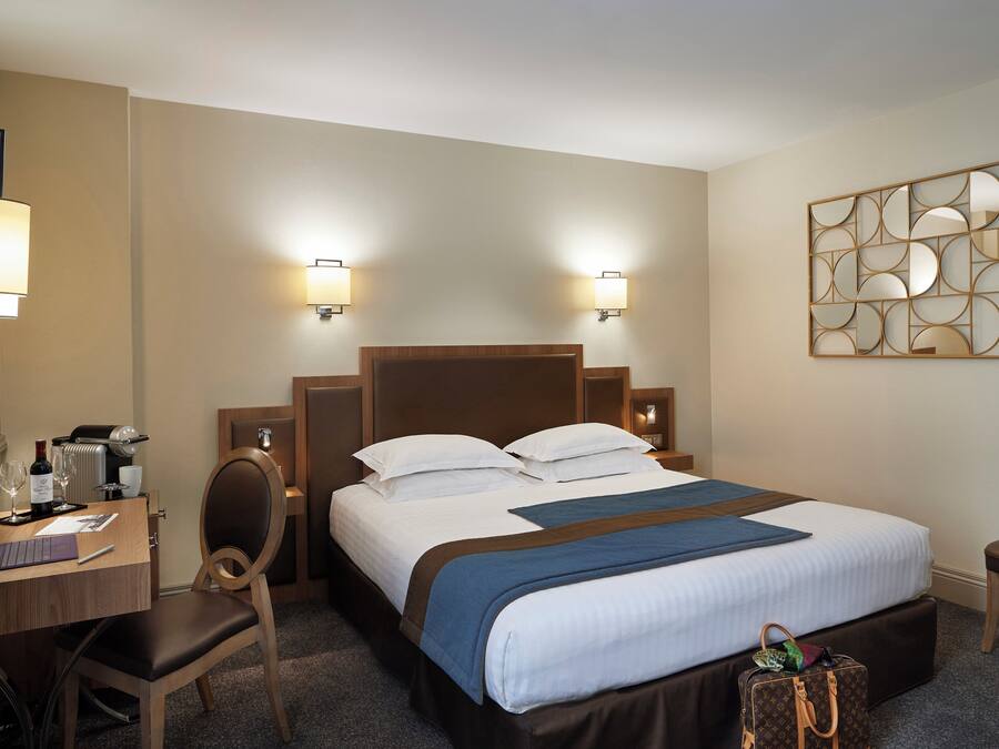 Una habitación de hotel con una cama, un escritorio, una silla, una lámpara y una obra de arte en la pared.