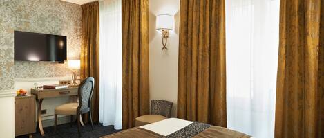 A hotel room with a bed, desk, chair, TV, and curtains.