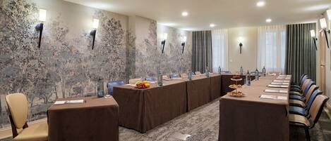 Un salón de conferencias con una mesa larga, sillas y una alfombra estampada.