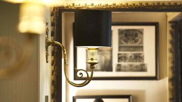 Un candelabro con pantalla negra y diseño decorativo, fijado en una pared con cuadros enmarcados al fondo.