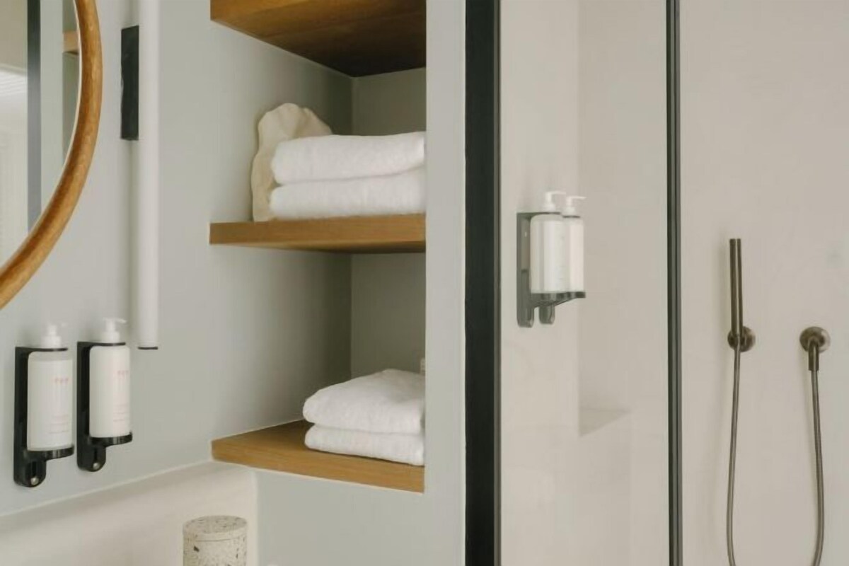 Ein Badezimmer mit Spiegel, Handtuchregalen, Dusche und Pflegeprodukten.