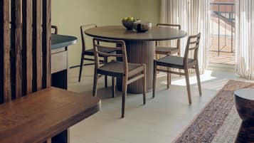 A dining area with a round table, chairs, a hanging light fixture, and a view of the outside through a window.