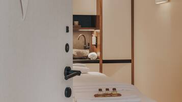 A modern hotel room with a bed, a bathroom with a sink, and a mirror.