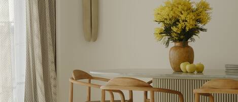 Une pièce comprenant une table à manger, quatre chaises, un vase avec des fleurs jaunes et une planche de surf accrochée au mur.