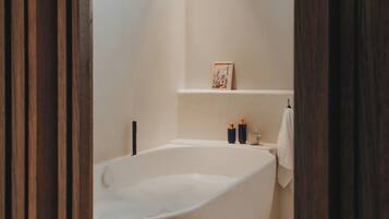 A modern bathroom with a freestanding bathtub, a towel rack, and a small shelf with toiletries.