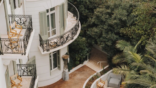 A multi-story building with a curved balcony, outdoor seating area, and lush greenery. - Hôtel & Spa Belle Plage (Cannes)