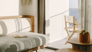 A modern living room with a sofa, a small table with a plant, a chair, and a large window with a view of the outdoors. - Hôtel & Spa Belle Plage (Cannes)