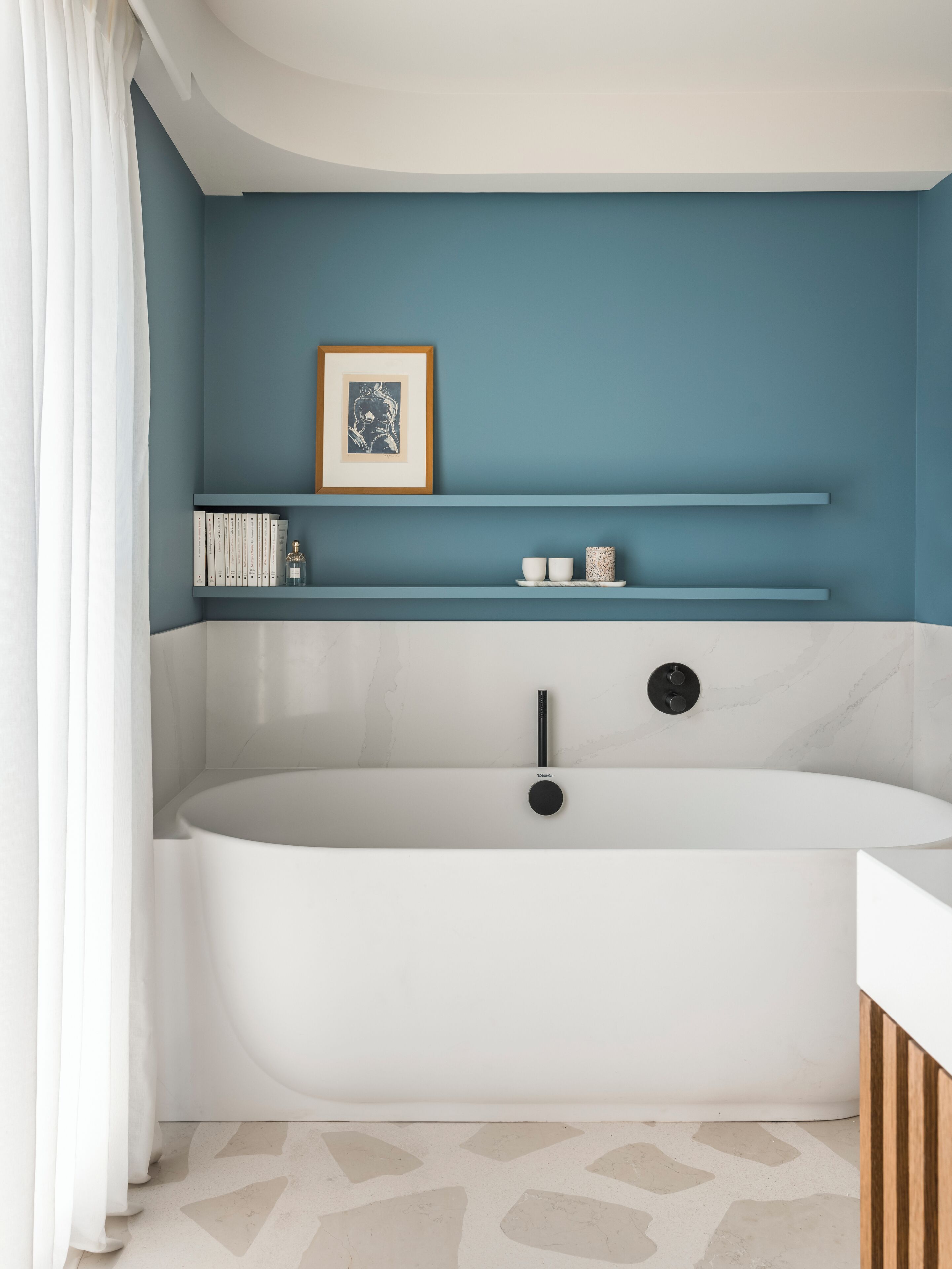 Une salle de bain moderne avec une baignoire sur pieds, un tableau encadré posé sur une étagère et un petit ensemble de produits de toilette.
