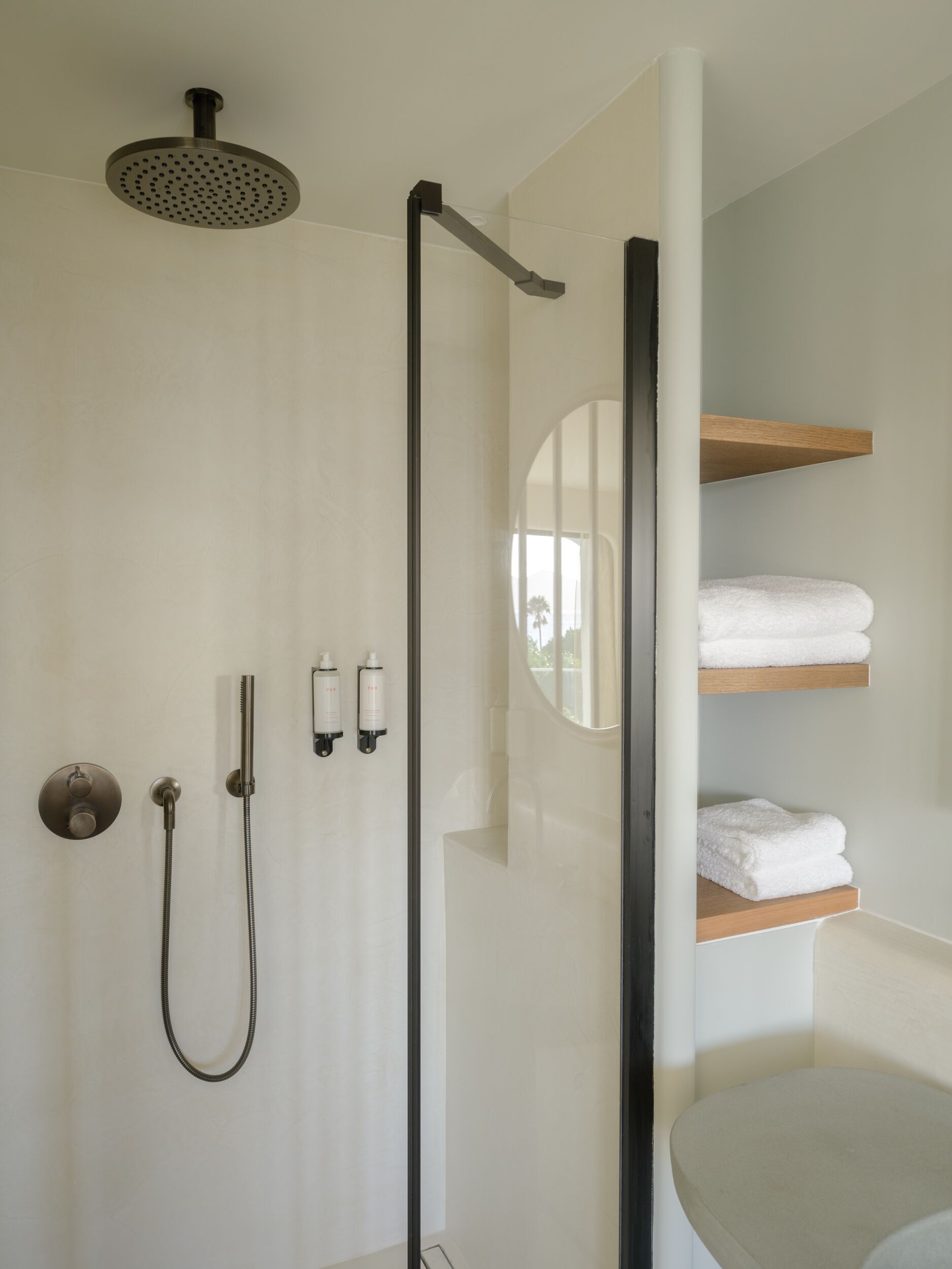A modern bathroom with a walk-in shower, a handheld showerhead, a handheld shower attachment, and two bottles of shampoo.