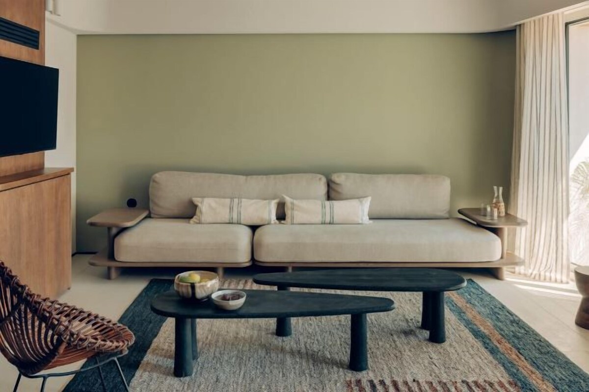 Ein Wohnzimmer mit einer Couch, einem Couchtisch, einem Korbstuhl und einem Fernseher.
