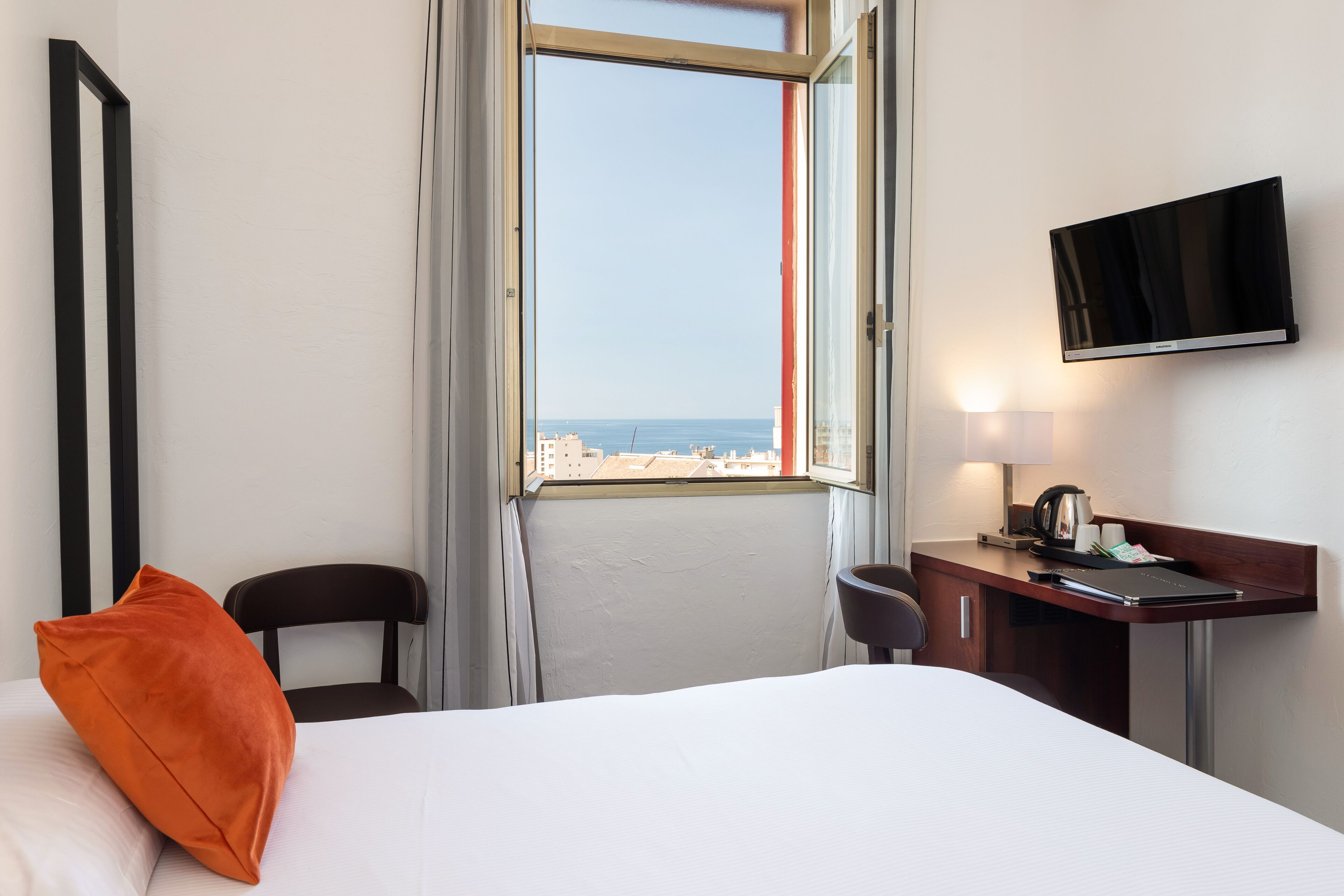 A hotel room with a bed, a desk, a chair, a TV, and a window with a city view.