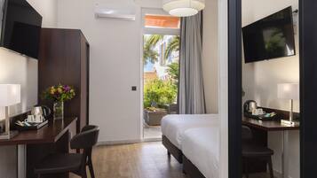 A hotel room with a bed, desk, chairs, a TV, and a view of an outdoor area with plants and a building.