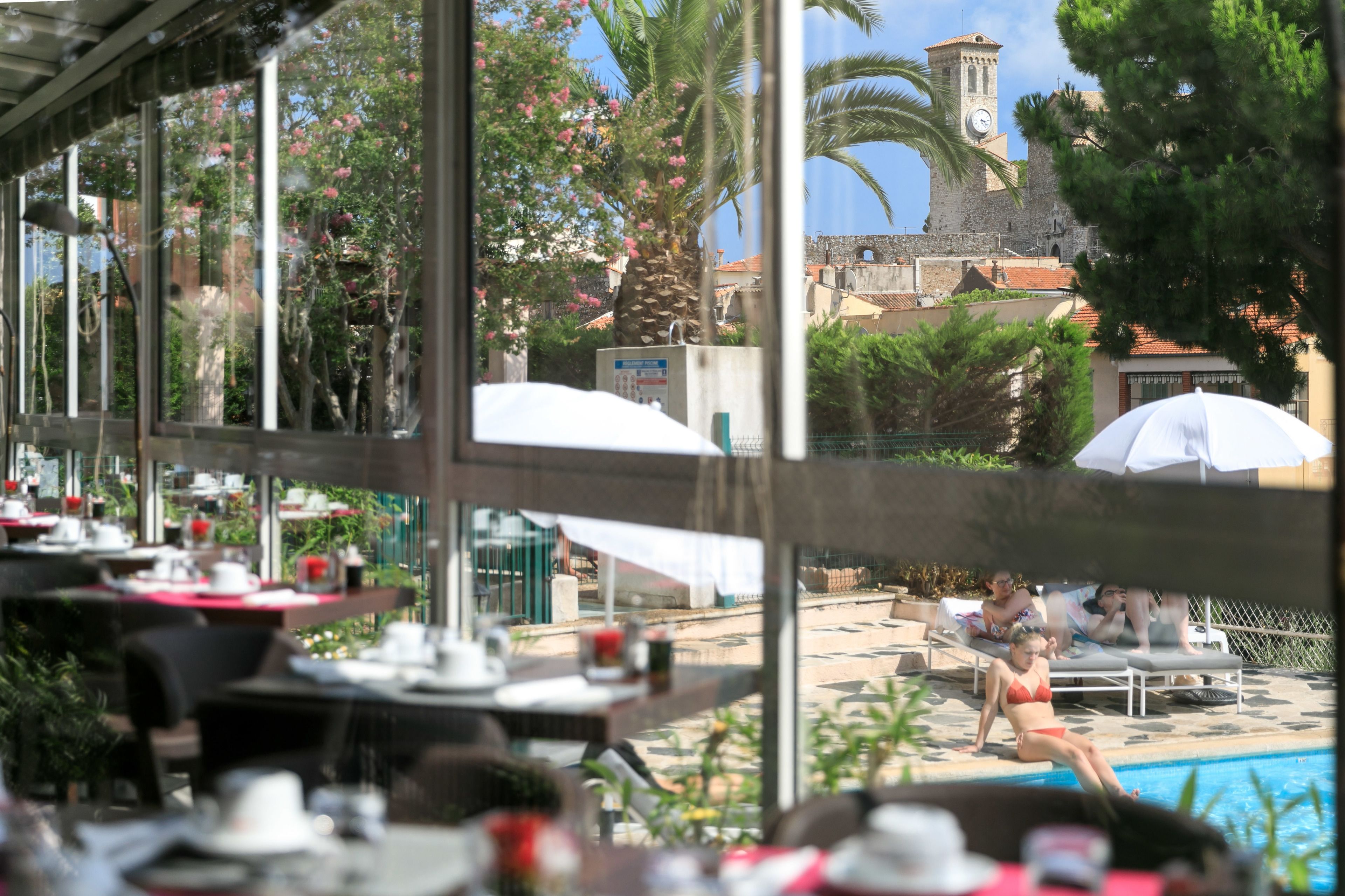 Un restaurante con terraza al aire libre que da a una piscina y un edificio histórico con una torre de reloj.