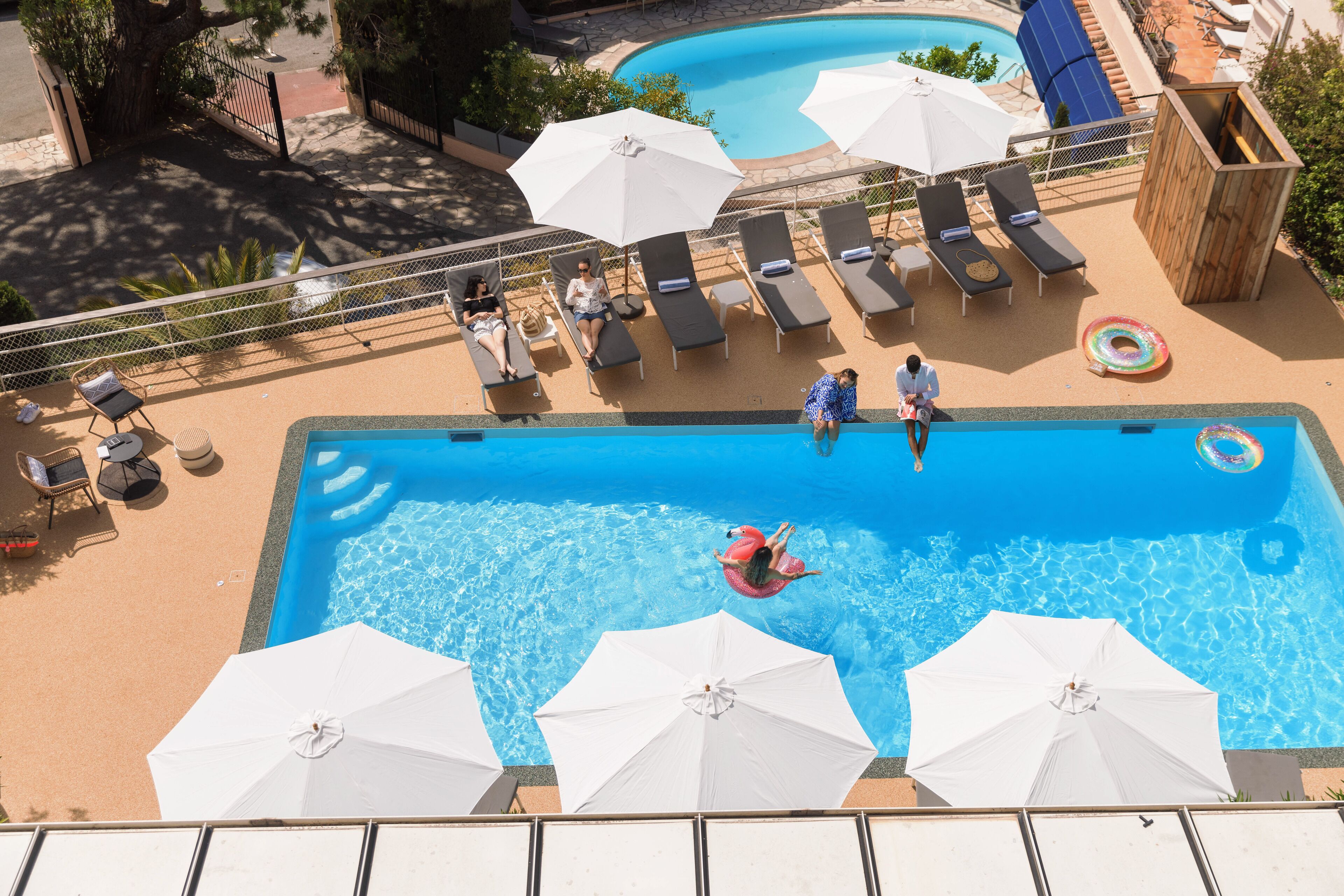 A swimming pool with lounge chairs and umbrellas, surrounded by a fence and trees.