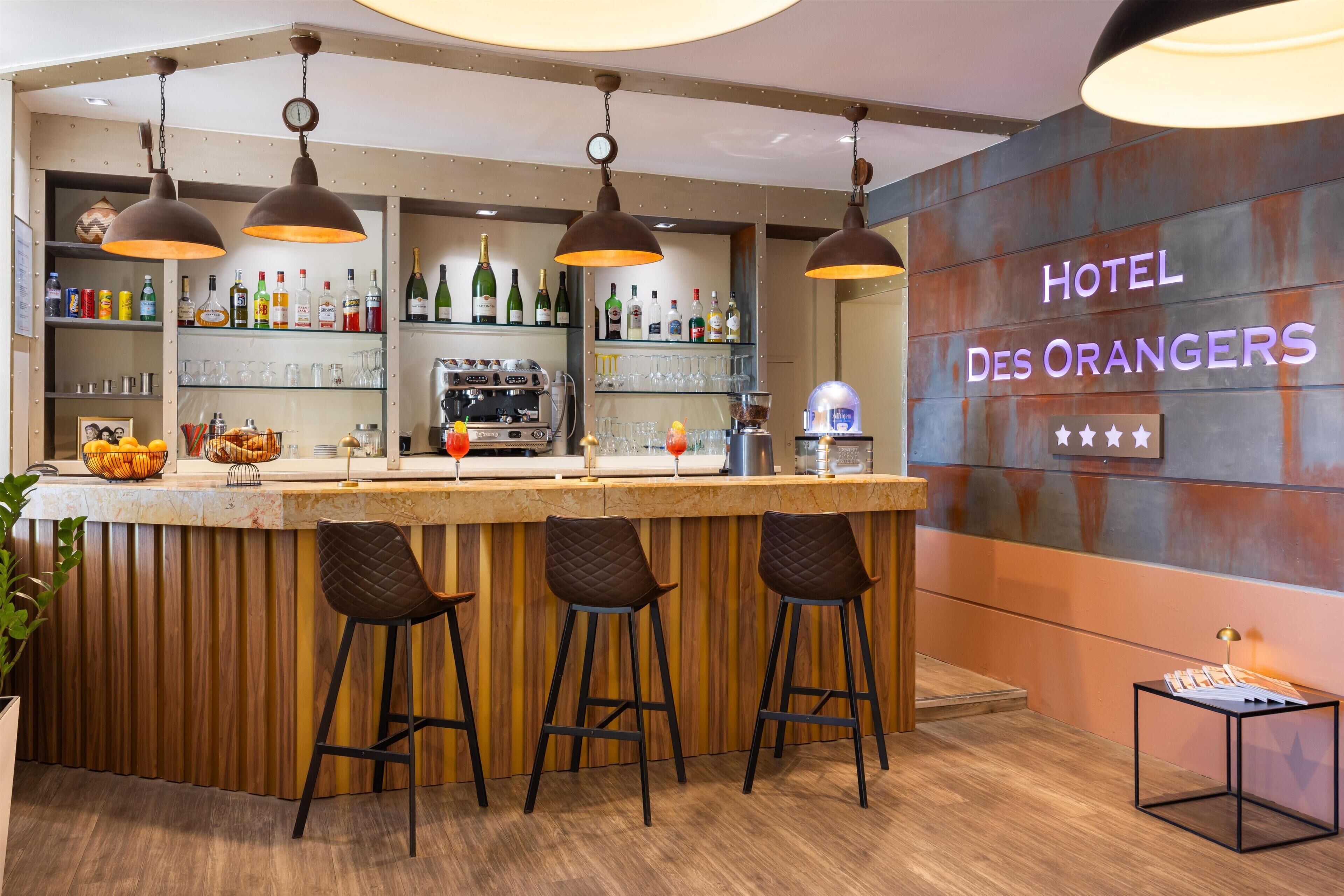 Zona de bar con taburetes de madera, lámparas colgantes y una barra repleta de botellas y vasos.