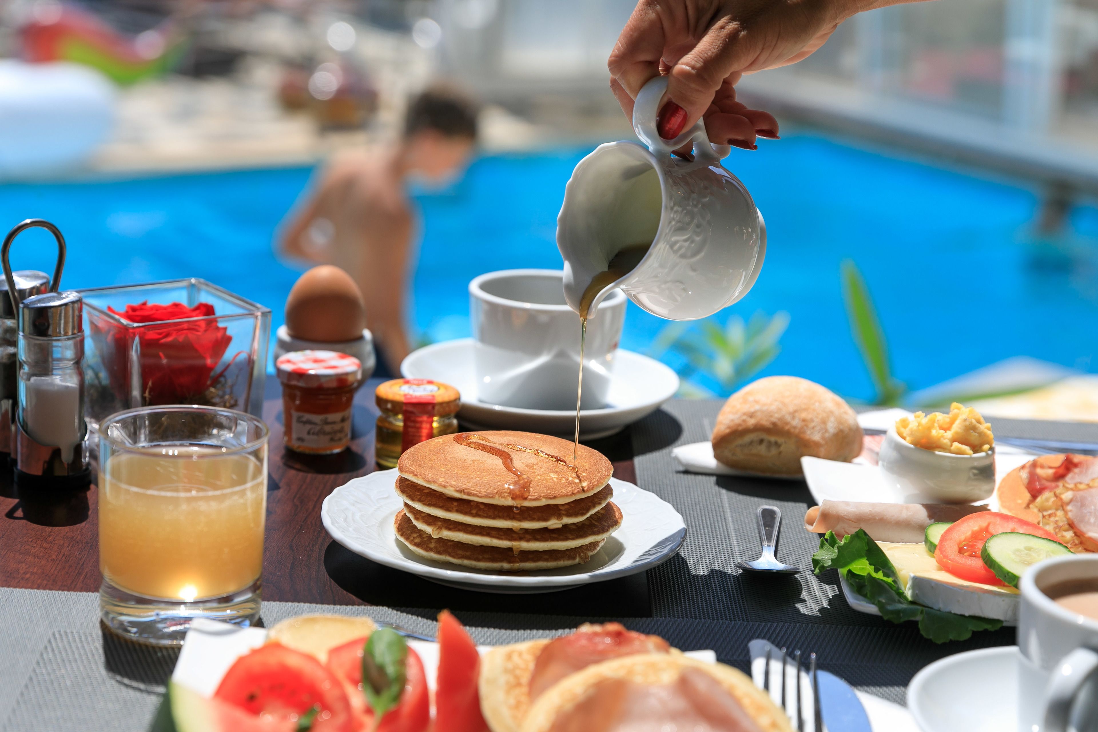 Une table de petit-déjeuner avec des crêpes, des œufs et une piscine en arrière-plan.