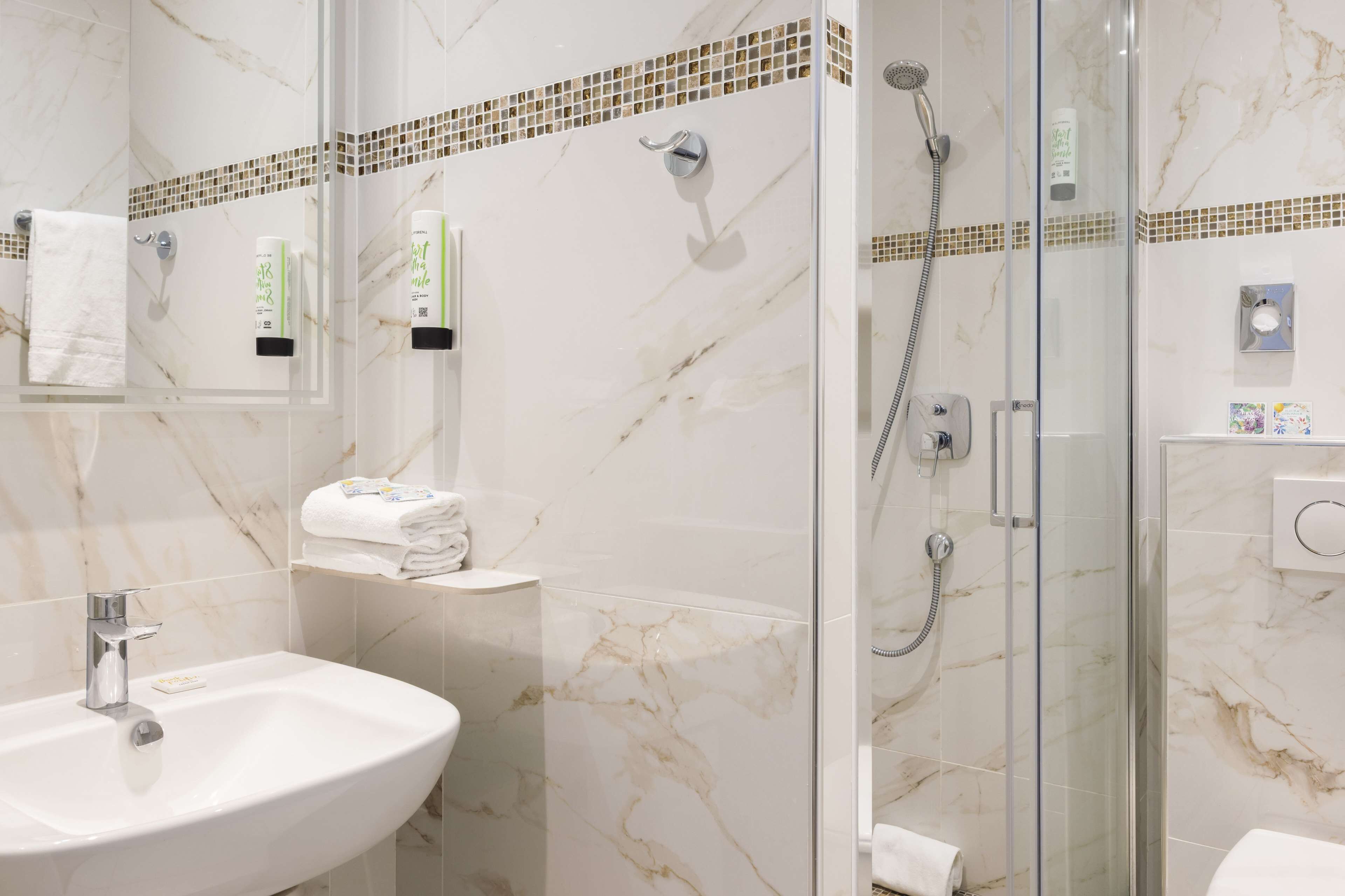 A bathroom with a marble sink, glass-enclosed shower, and a tiled backsplash.