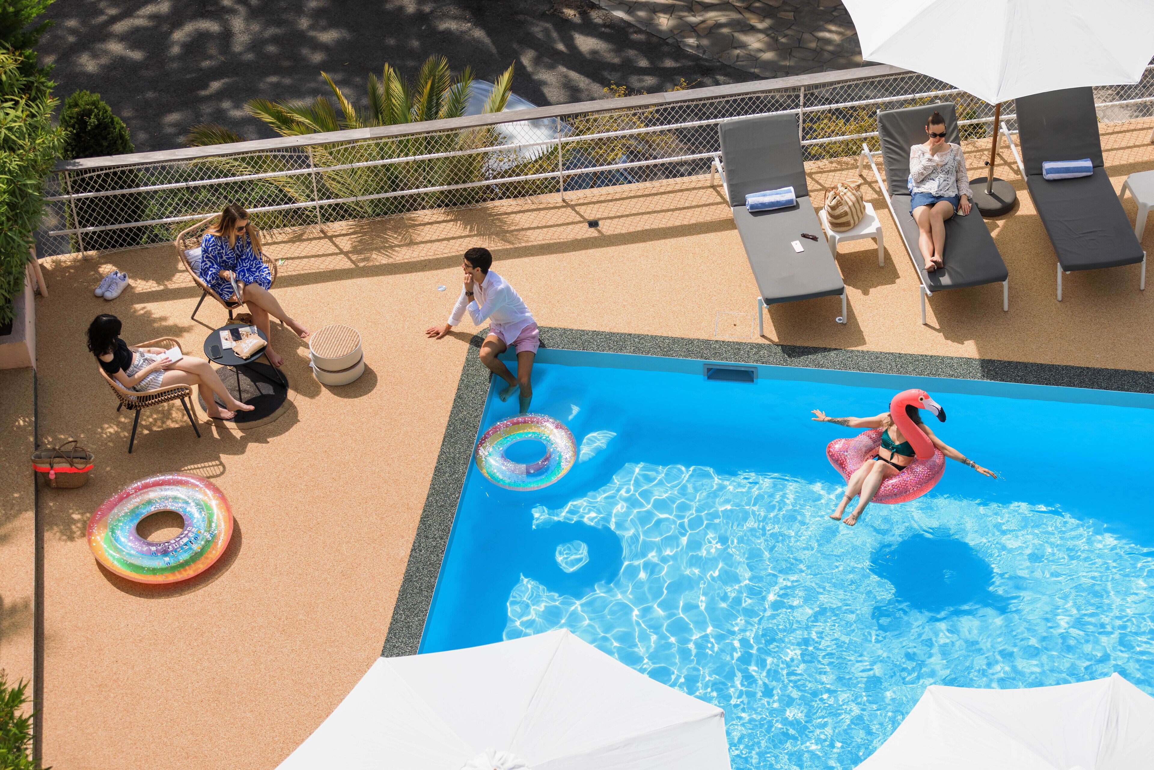 A poolside area with lounge chairs, a swimming pool, and a person in a pink flamingo float.