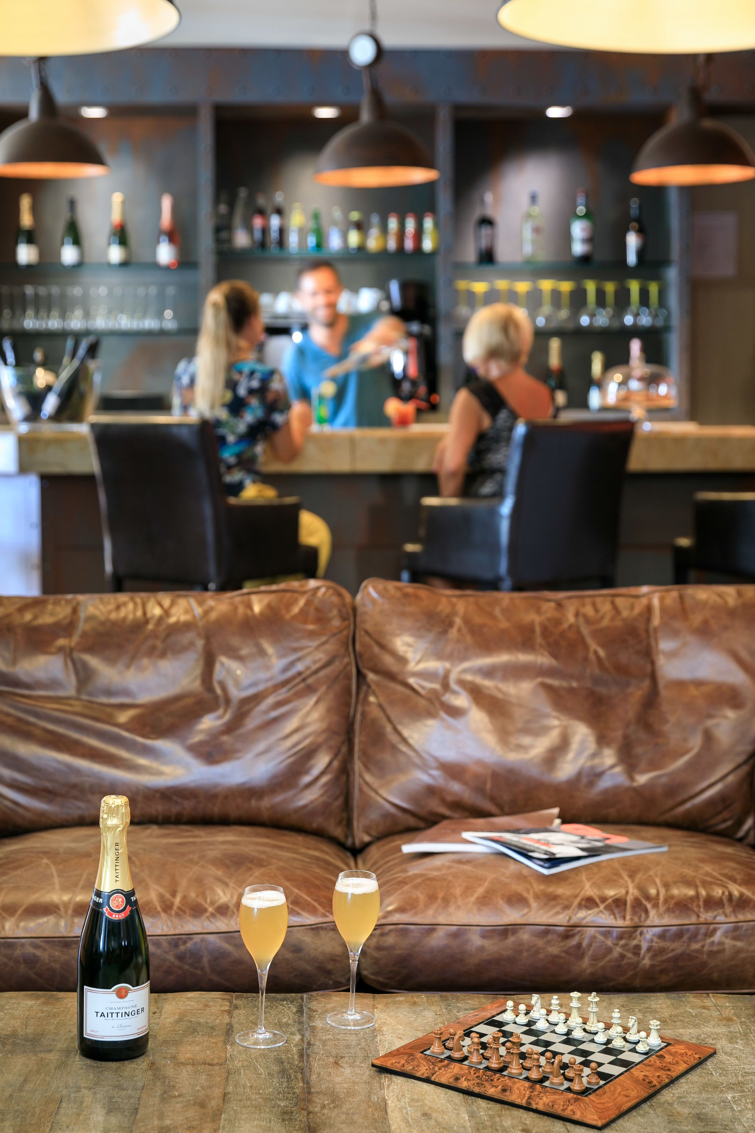 Eine Barbereich mit einer Ledersofa, einer Flasche Taittinger Champagner und zwei Champagnergläsern auf einem Holztisch.