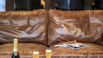 Eine Barbereich mit einer Ledersofa, einer Flasche Taittinger Champagner und zwei Champagnergläsern auf einem Holztisch.
