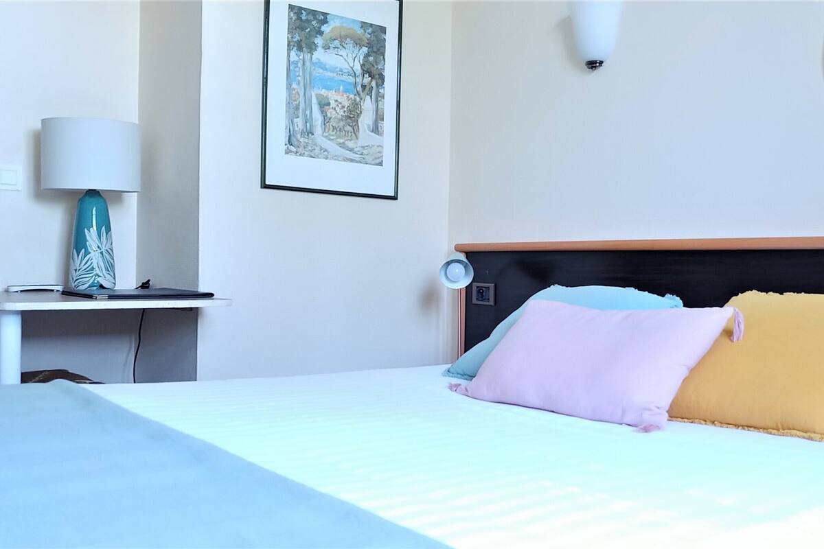 Ein Hotelzimmer mit einem Bett, einem Nachttisch mit Lampe und einem gerahmten Bild an der Wand.