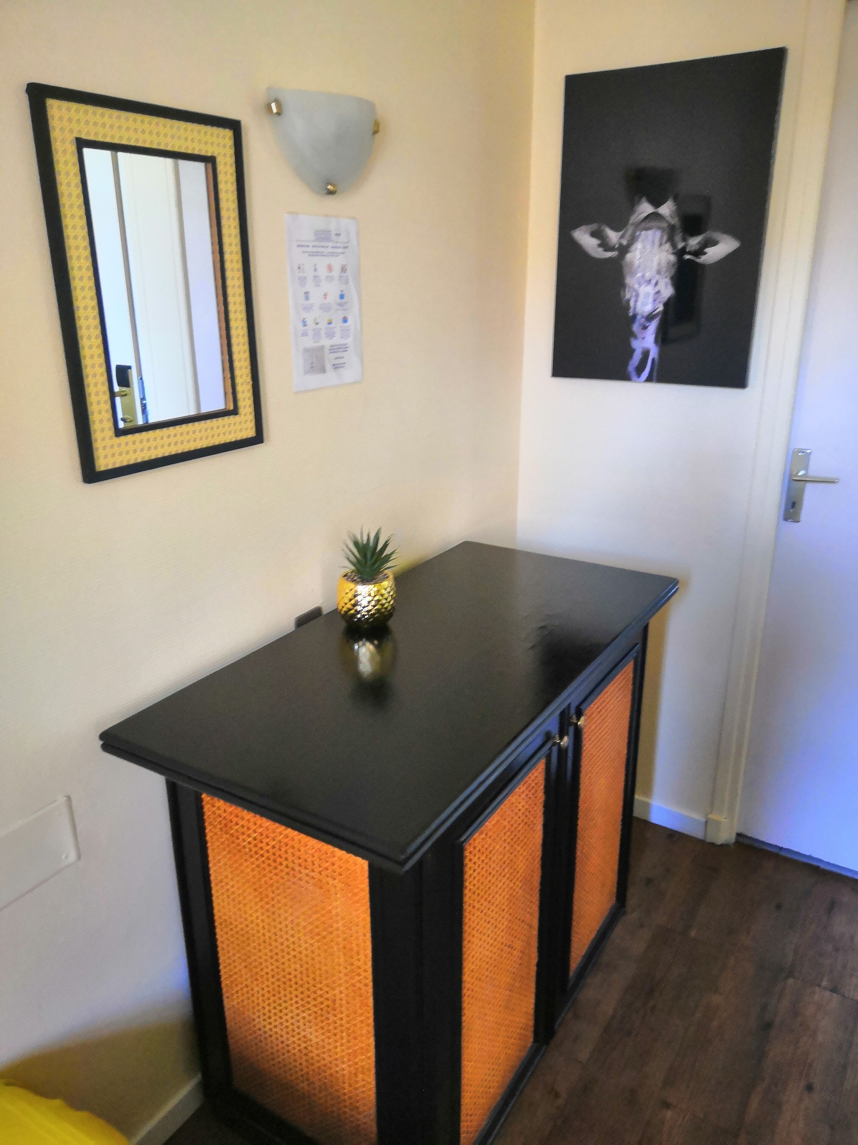 A small room with a black table, a mirror, a wall-mounted light, and a framed picture.