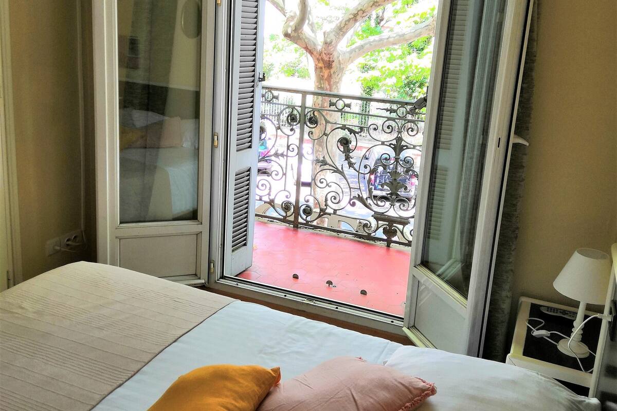 Ein Schlafzimmer mit Bett, Kissen, einem Fernseher und einem Fenster mit Balkonblick.