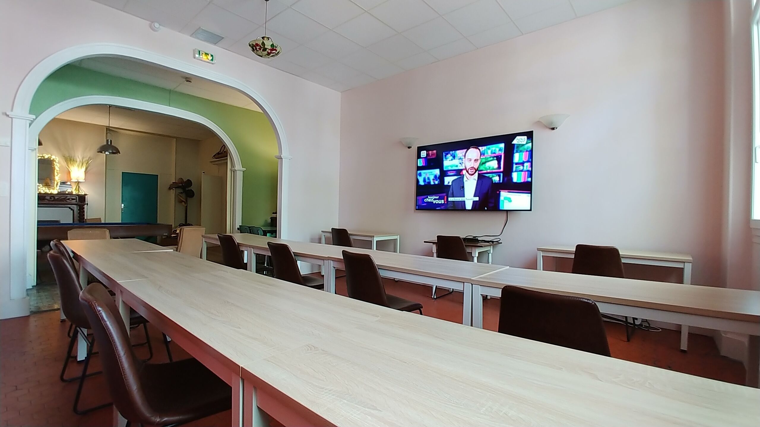 A conference room with a long table, chairs, a television screen, and a green archway.