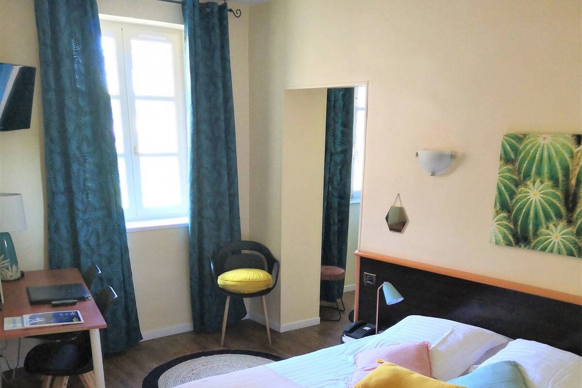 Ein Schlafzimmer mit einem Bett, einem Schreibtisch, einem Stuhl und einem Fenster mit Vorhängen.
