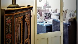 Une pièce avec un meuble en bois, un tableau encadré et une vue, par une grande fenêtre, sur un espace de vie comprenant un canapé, des coussins et un coussin à motifs zébrés.