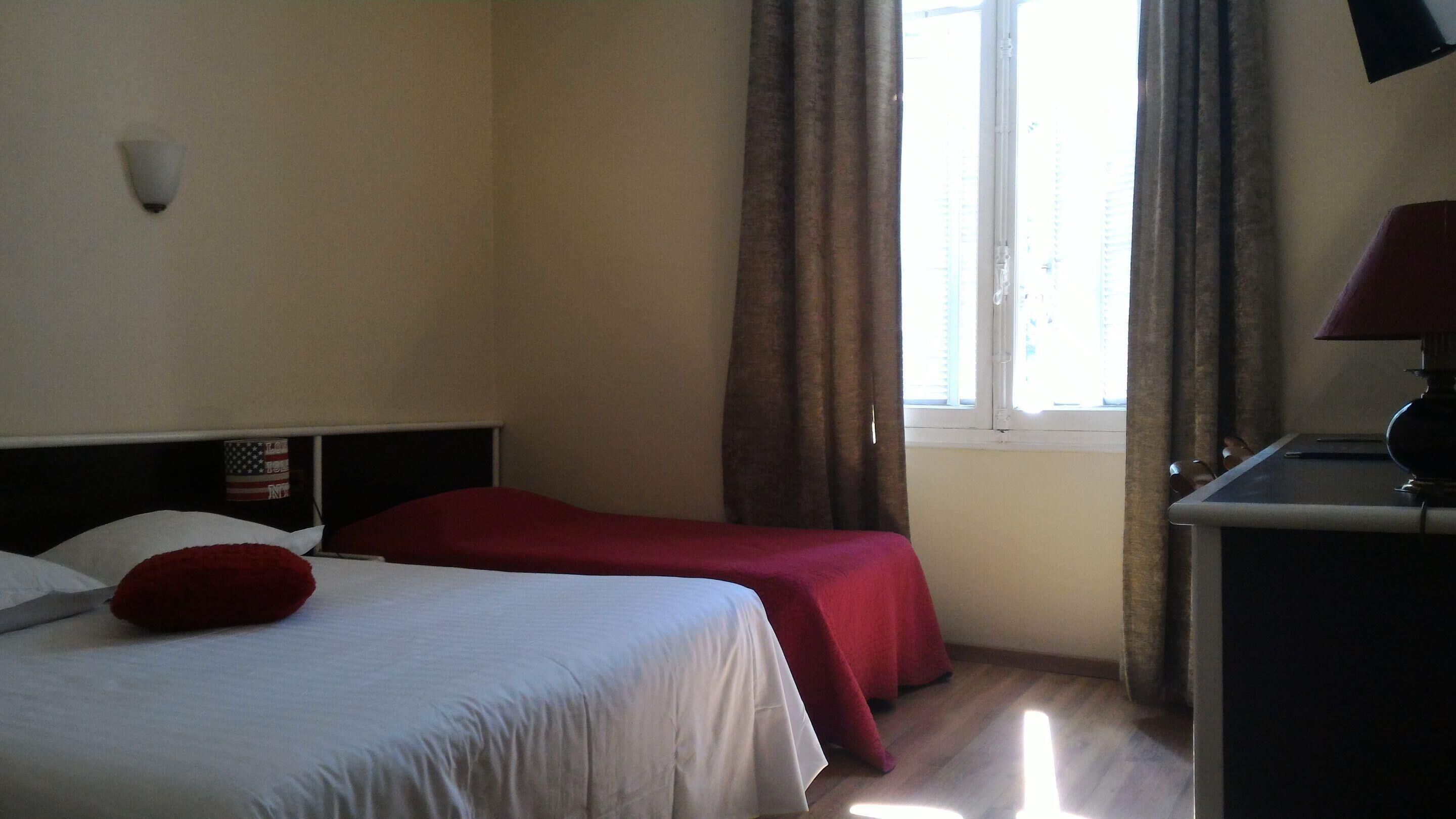 Habitación de hotel con dos camas, una ventana con cortinas, un escritorio con lámpara y una lámpara en la pared.