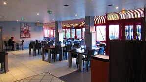 A restaurant with multiple tables and chairs, a tiled floor, and a ceiling with recessed lighting. - Hotel Gallieni (Gennevilliers)
