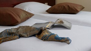 A neatly made bed with white sheets, two brown pillows, and a magazine on the bed. - Hotel Gallieni (Gennevilliers)