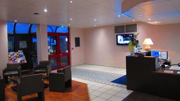 A lobby with a reception desk, seating area, and a door leading to a hallway. - Hotel Gallieni (Gennevilliers)