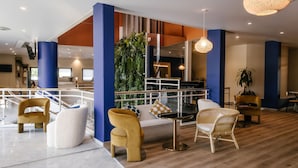 A modern lounge area with a wooden floor, white and yellow chairs, a sofa, and a green vertical garden. - 7Hotel&Spa (Illkirch-Graffenstaden)