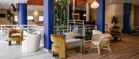 Un'area lounge moderna con pavimento in legno, sedie bianche e gialle, un divano e una parete verde verticale.