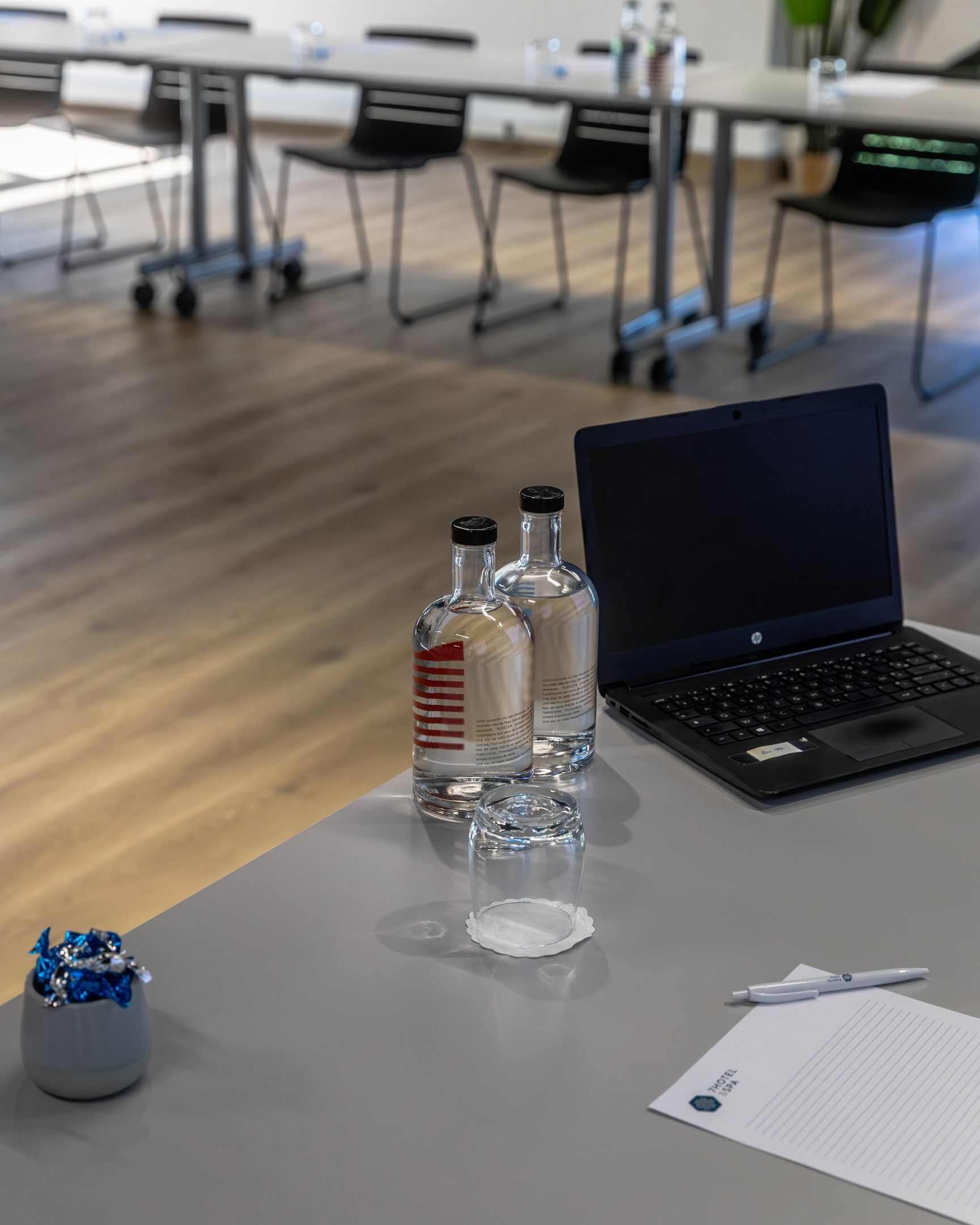 A conference table with a laptop, two bottles of water, a glass, a pen, and a notepad in a modern office setting.