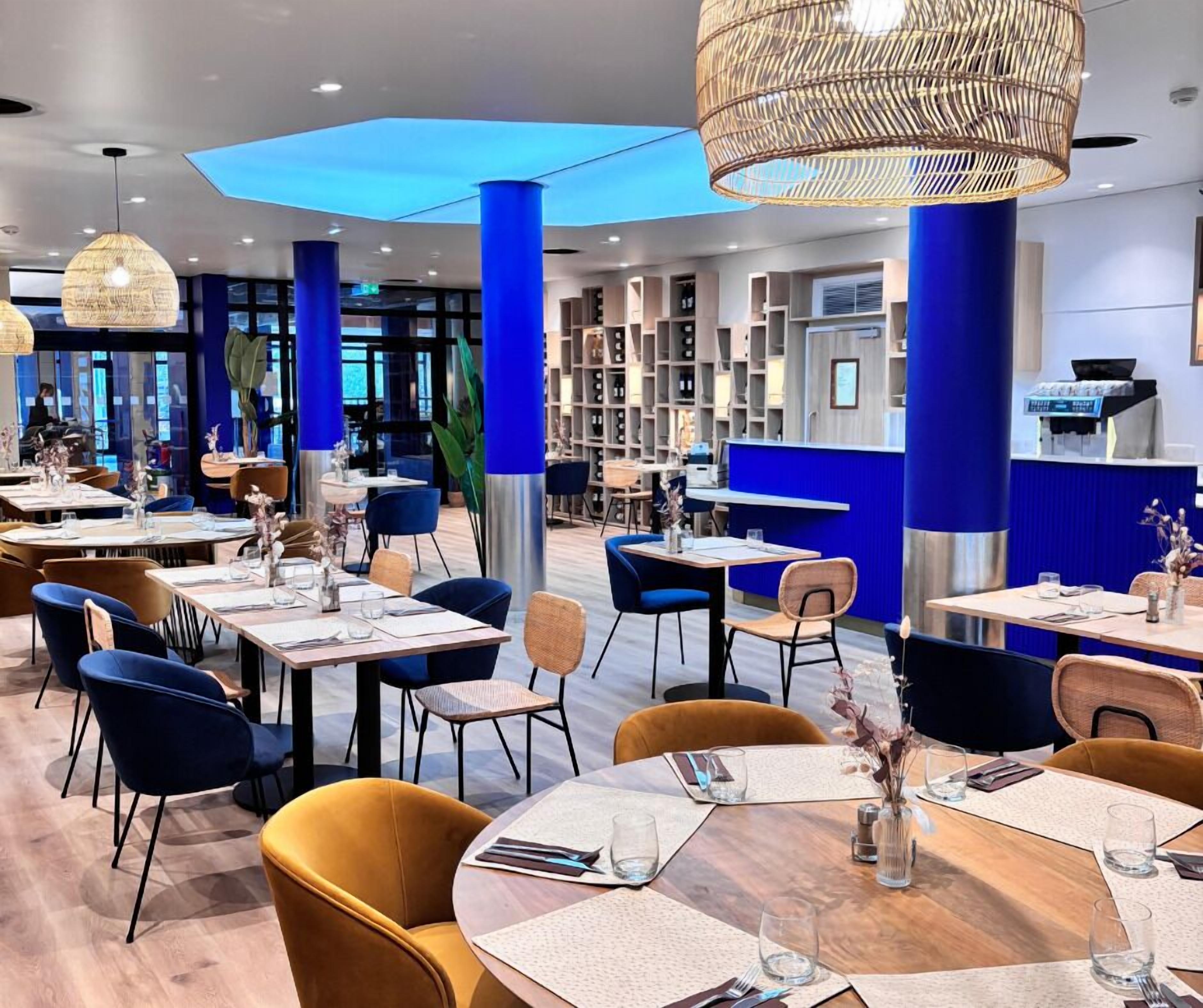 Ein modernes Restaurant mit blauen Akzenten, runden Tischen und Korbtablets als Pendelleuchten.
