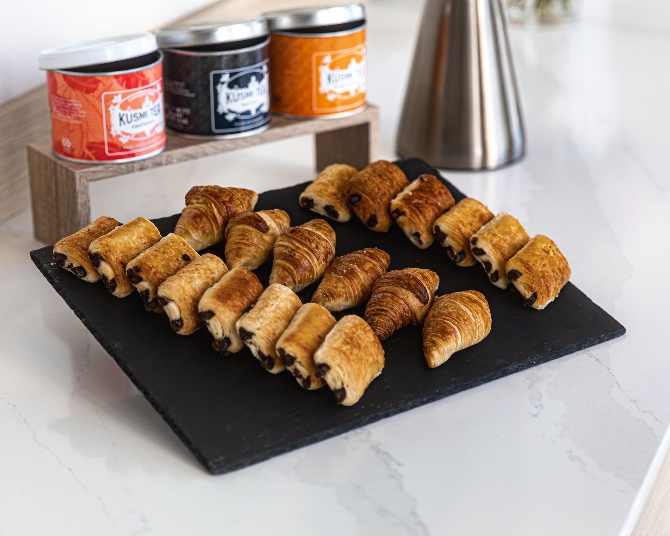 A black slate board with assorted pastries, including croissants and chocolate-filled pastries, on a marble countertop.