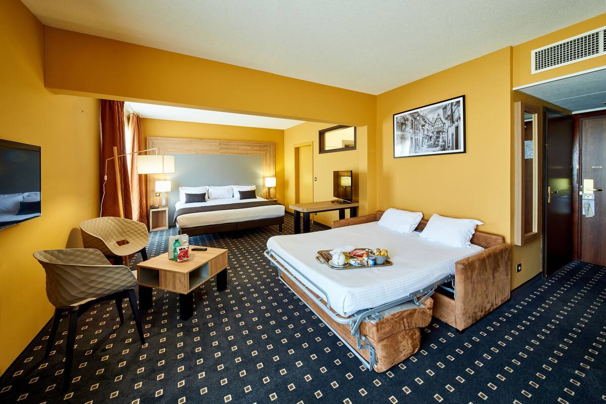 A hotel room with a bed, a desk, a chair, a bedside table, and a TV.