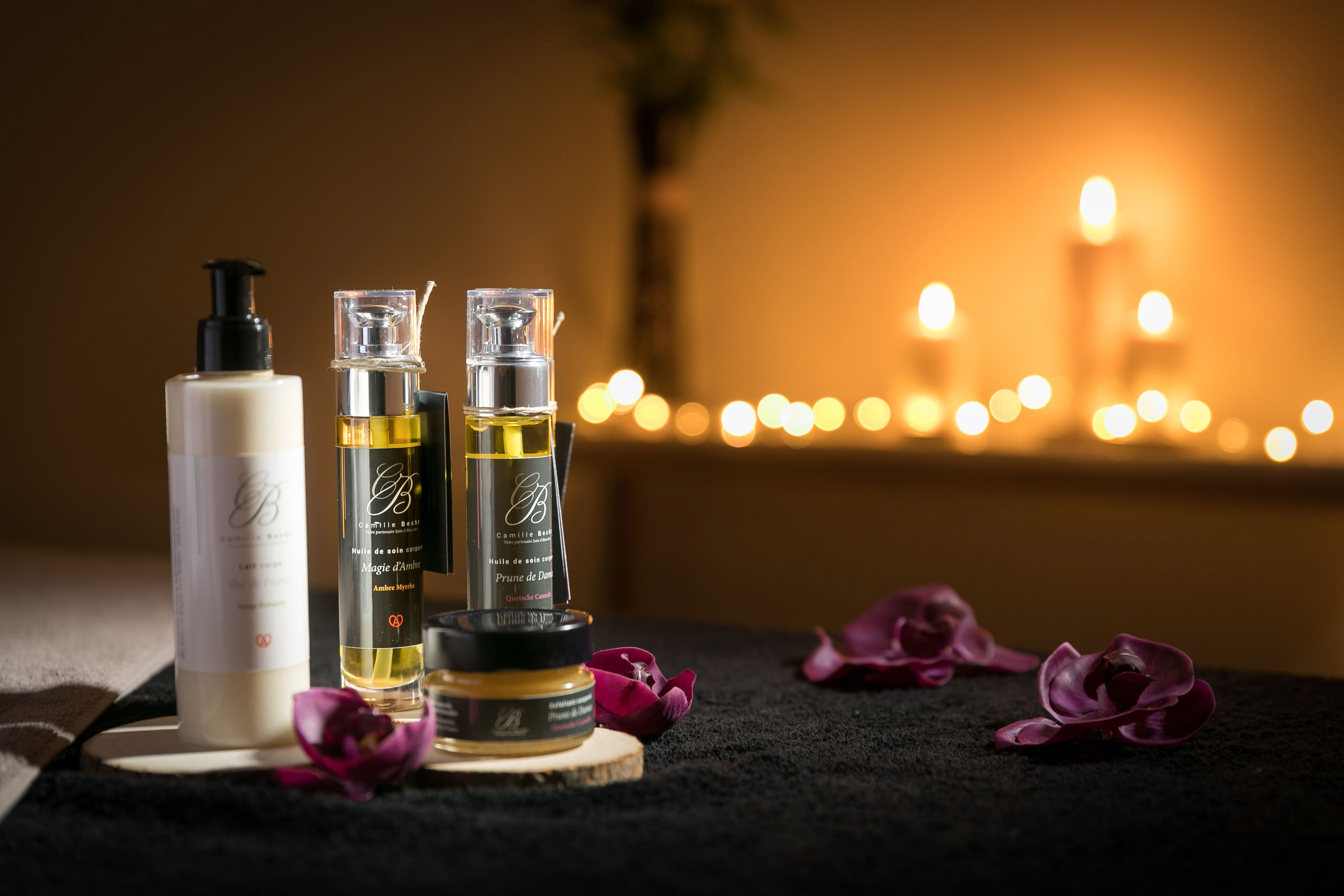Trois flacons de parfum sur un plateau en bois, avec une bougie en arrière-plan.