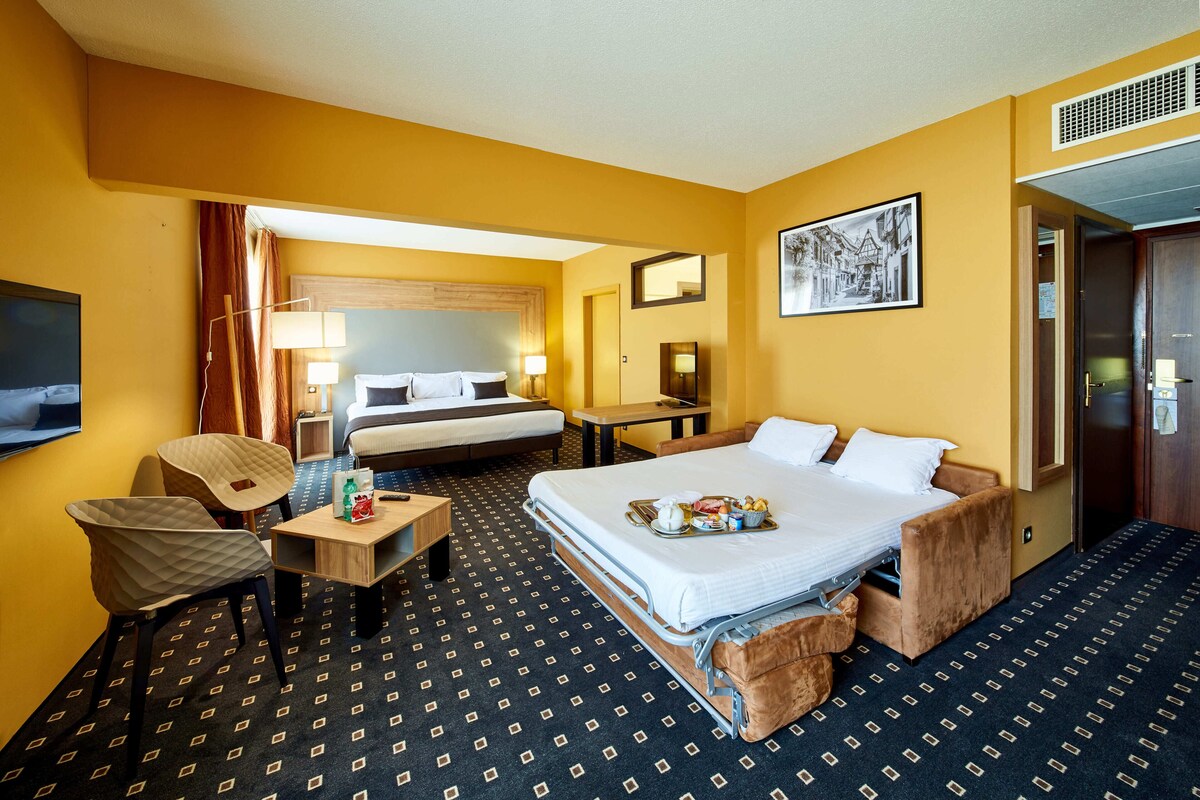Une chambre d’hôtel comprenant un lit, des tables de chevet, un bureau, une chaise et un téléviseur.