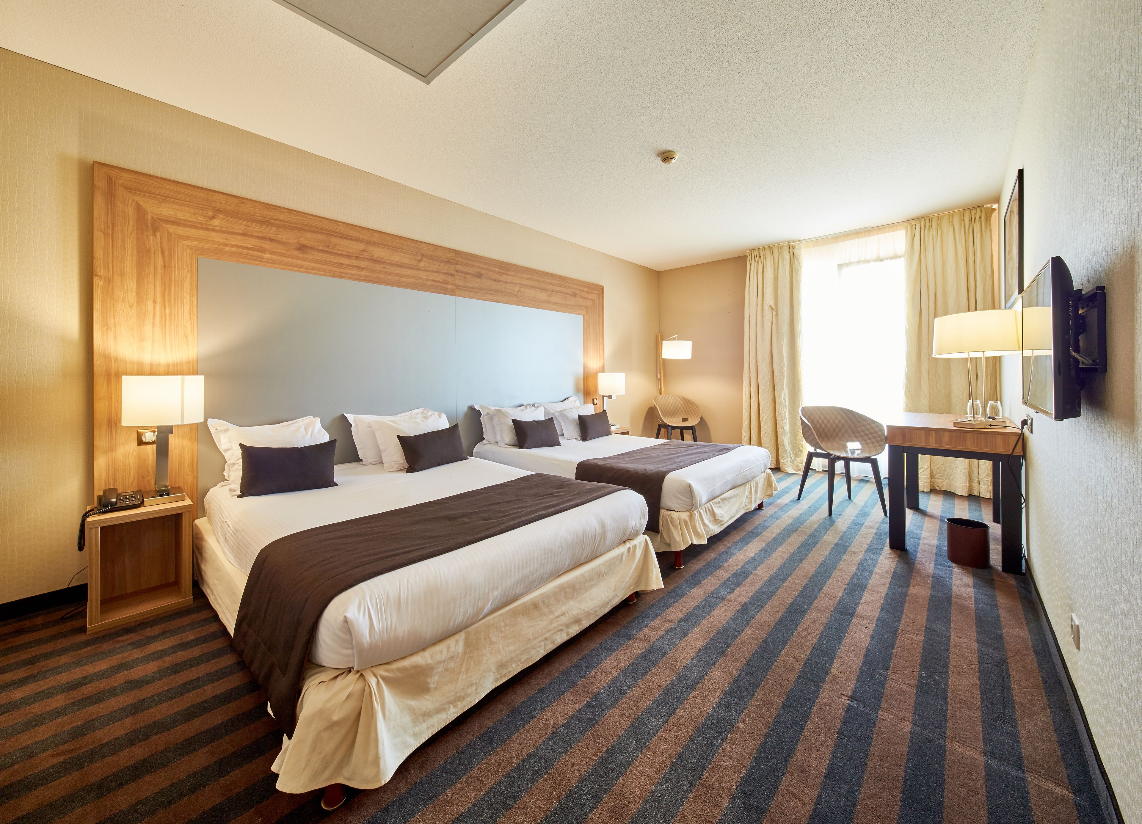 Ein Hotelzimmer mit zwei Betten, einem Schreibtisch, einem Sessel, einem Fernseher und einem Telefon.