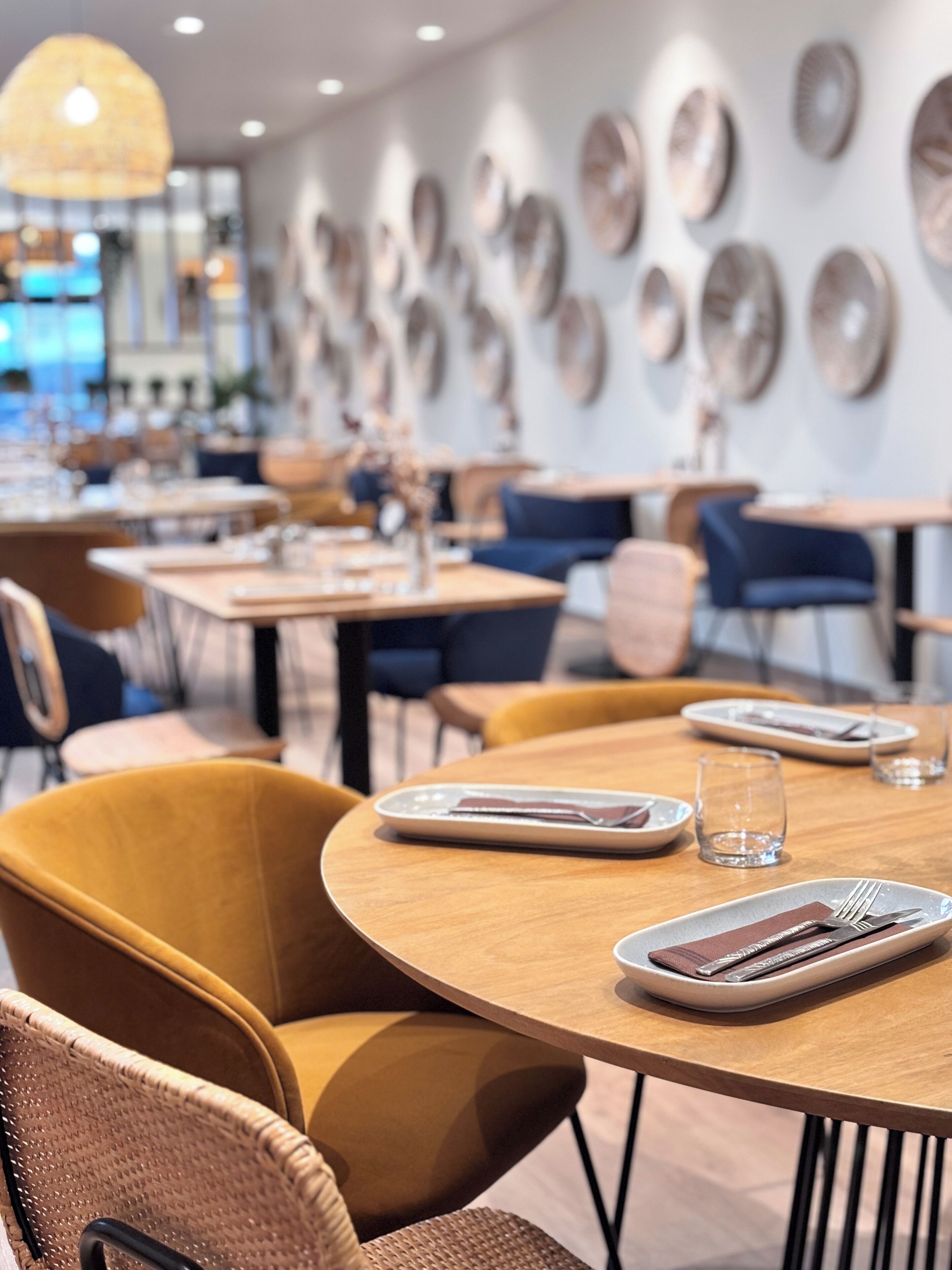 A modern dining area with round tables, wicker chairs, and a decorative wall with circular patterns.