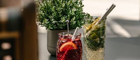 Two drinks on a table with a potted plant in the background.