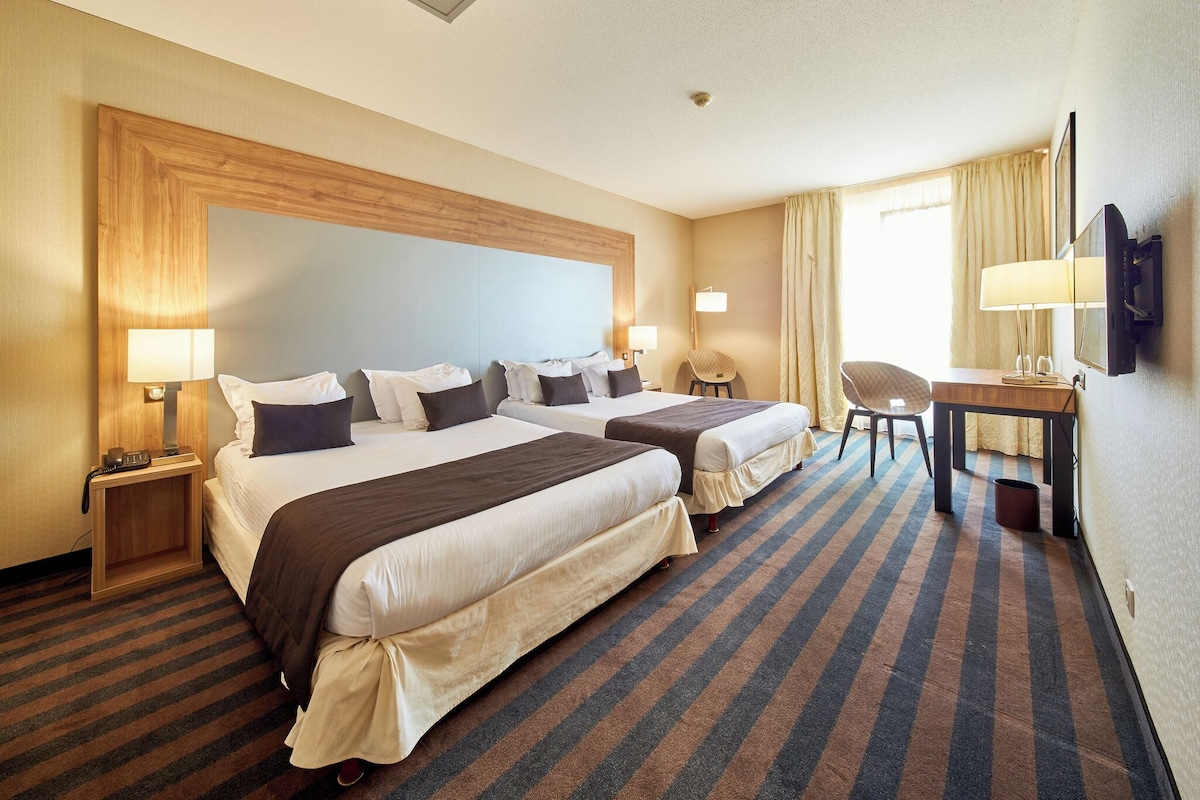 Une chambre d’hôtel avec deux lits, un bureau, une chaise et un téléviseur.