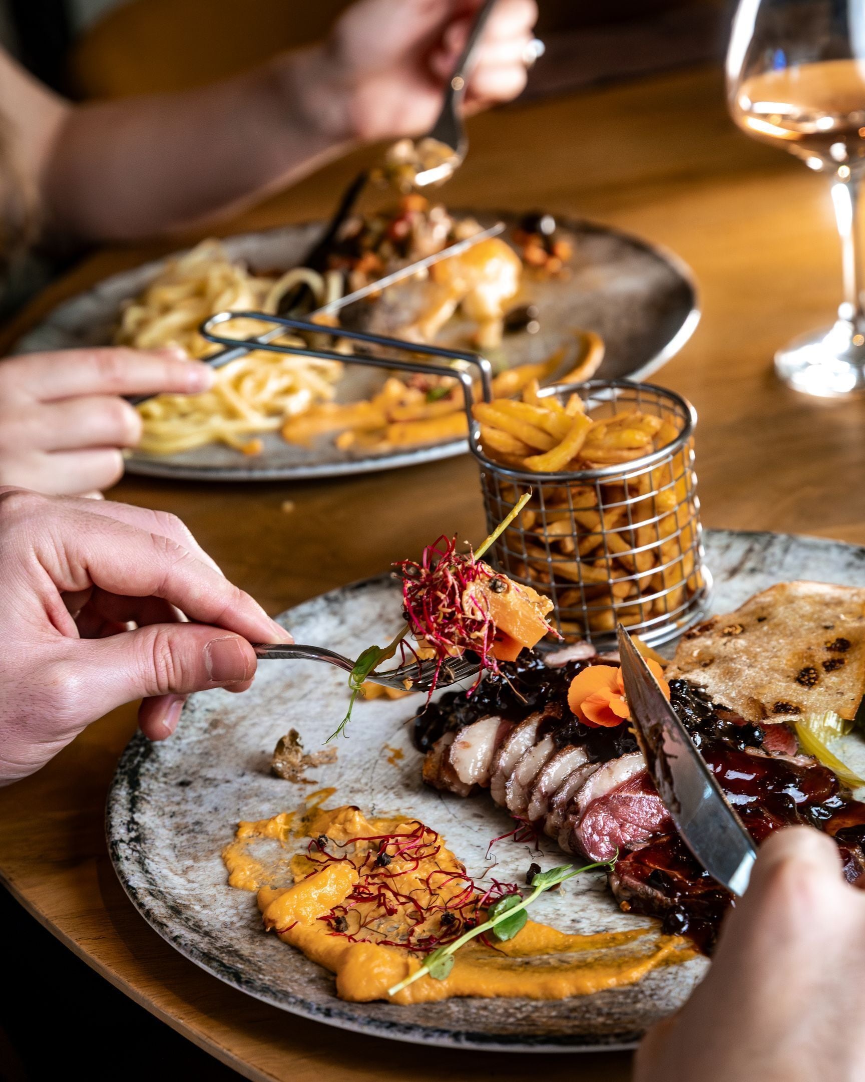 A dining table with plates of food, a glass of wine, and a metal basket.