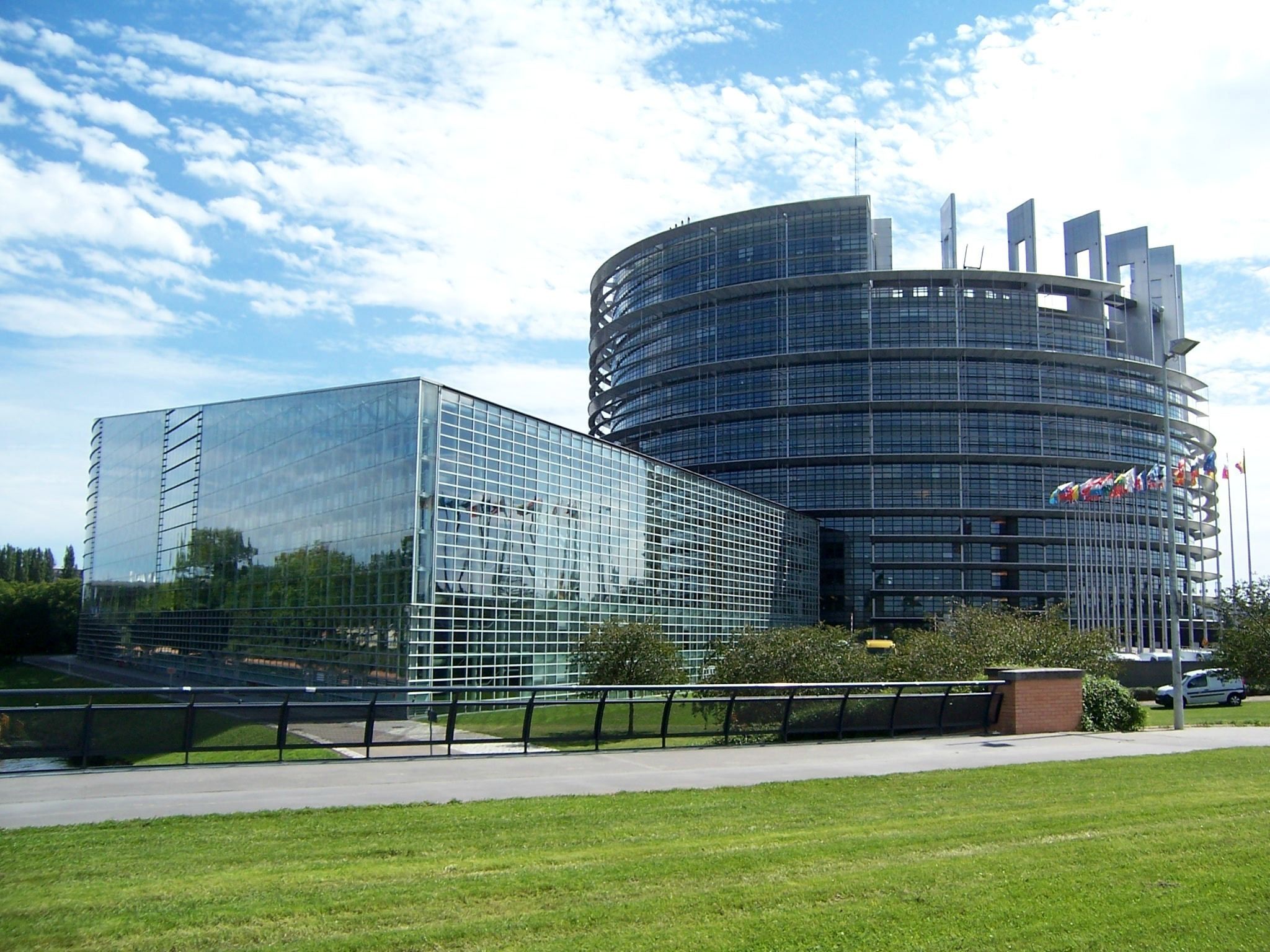 A modern building with a glass facade and a cylindrical section, surrounded by a well-maintained lawn and a metal fence.