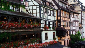 A traditional half-timbered building with multiple stories, balconies with red flowers, and a steeply pitched roof. - 7Hotel&Spa (Illkirch-Graffenstaden)