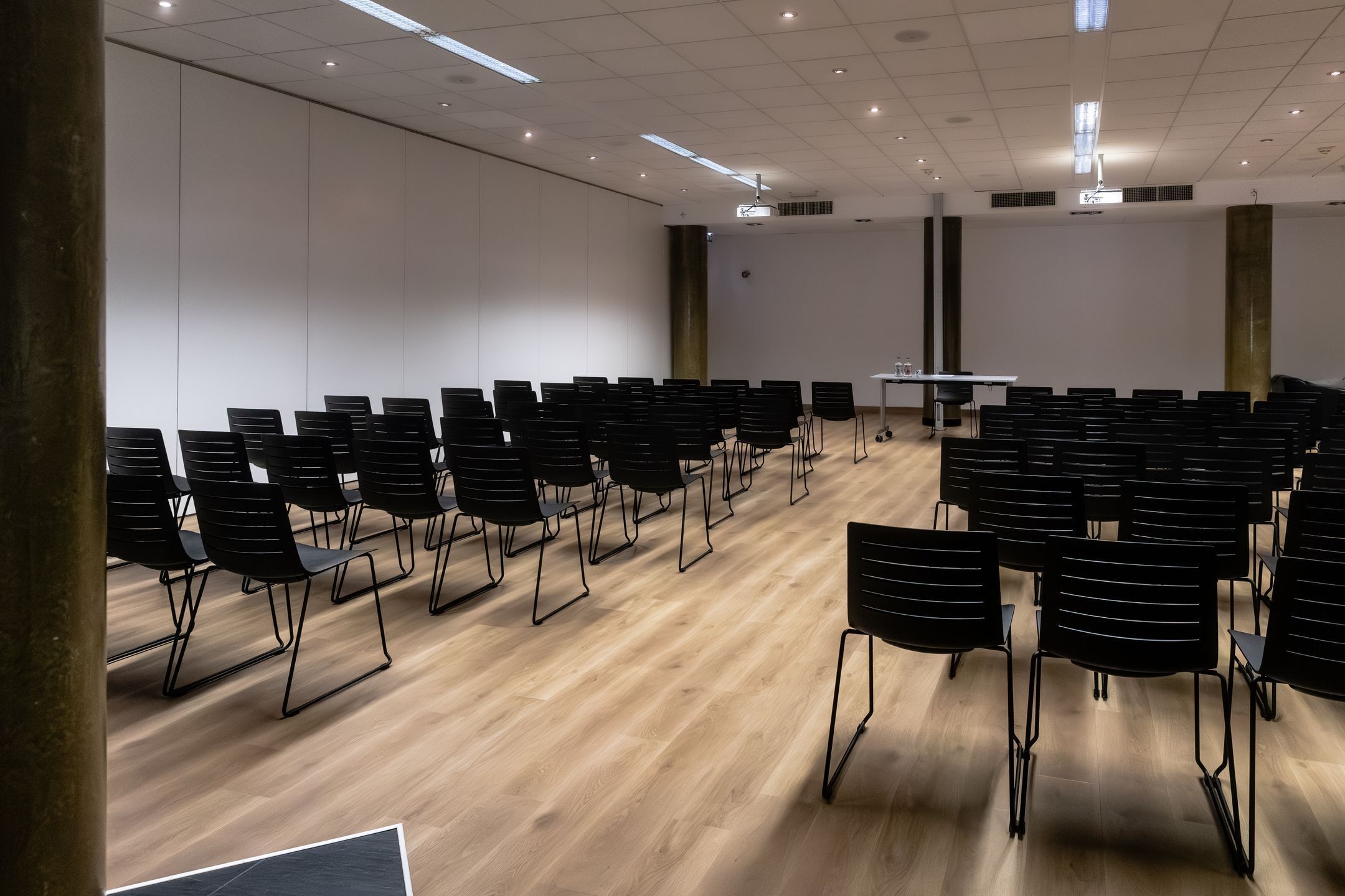 A conference room with rows of black chairs, a white table, and a projector screen.